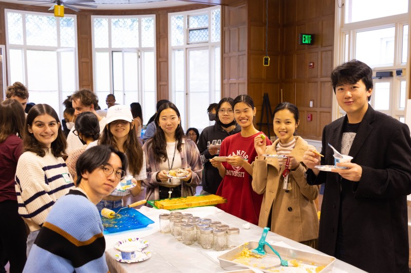 Students smiling, gathered around a table, eating honey and other snacks.