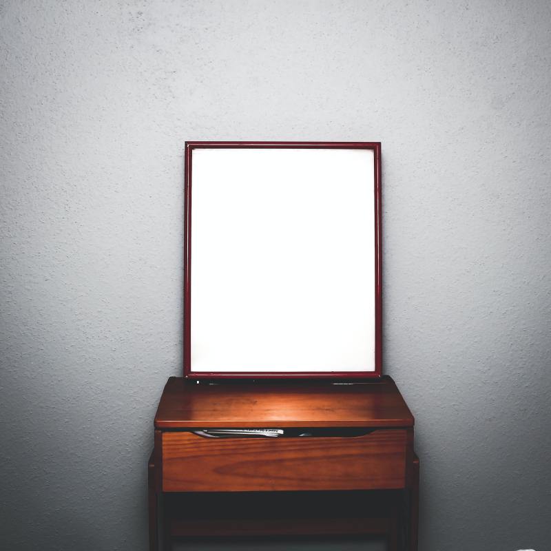 A mirror that stands on a desk in an empty room.