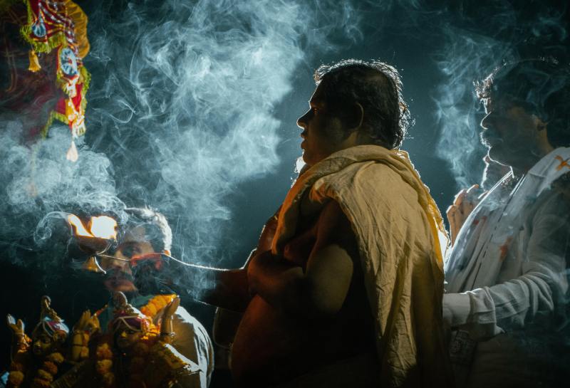 It is dark out, and Hindu priest conducting a religious havan. There are two other religious officers in front and behind.