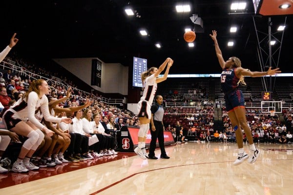 A women's basketball player in a white uniform takes a jump shot