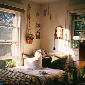 A bed sits next to a window with various decorations on the wall.