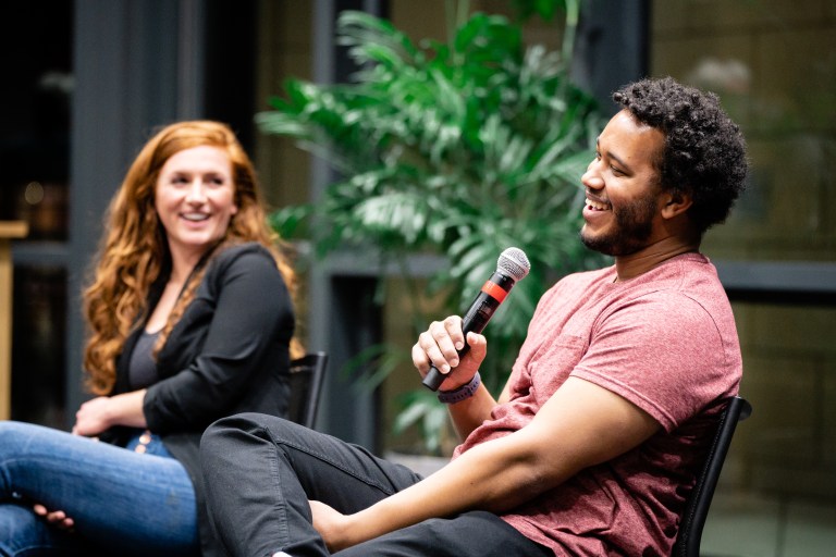 A red-haired woman and a man in a pink shirt laugh and speak to the audience