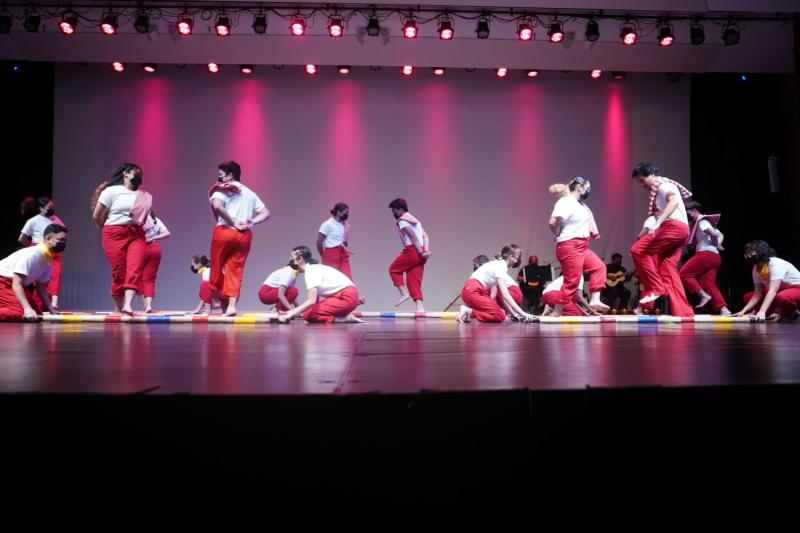 A group of dancers wearing white shirts and red pants doing the tinikling dance