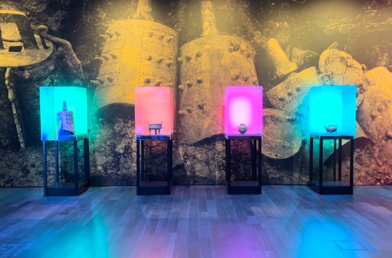 Four objects from the Warring States period are displayed in cases illuminated by neon light.