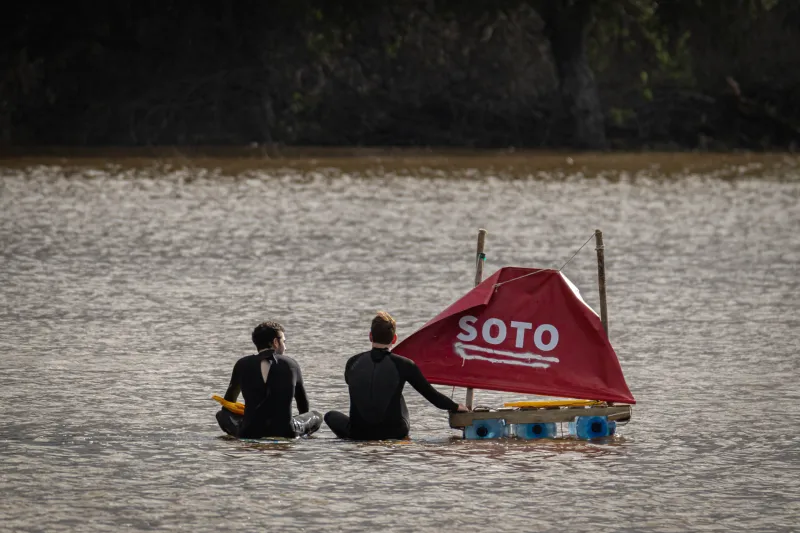 Two students sit with a red Soto flag in the middle of the lake.