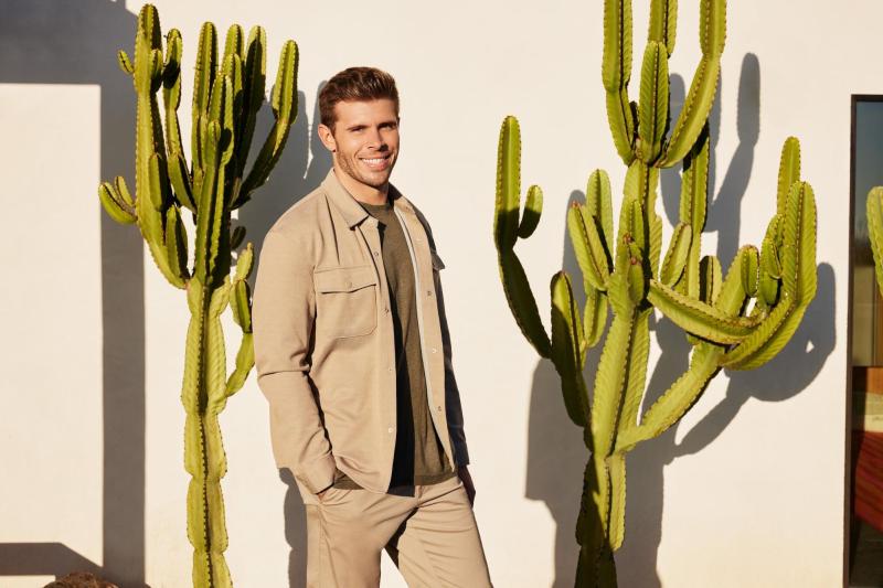 A young man standing in between two cactus plants.