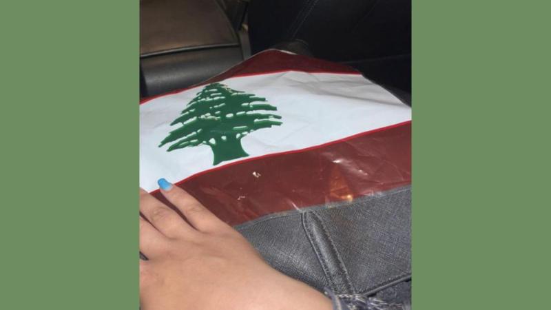 A Lebanon flag laying on a flat surface with a hand touching it.
