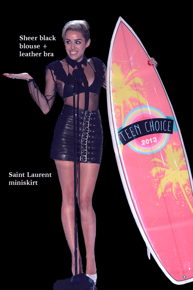 a photo of a white person with short blonde hair, wearing a seethrough black top and tight, shiny black skirt. the person is holding up a pink surfboard with the text "Teen Choice 2013" printed on.