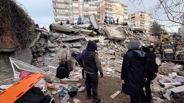 People facing the wreckage of a collapsed building after an earthquake.