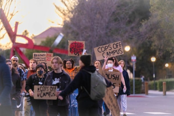 Student protestors hold signs and walk in orange light.