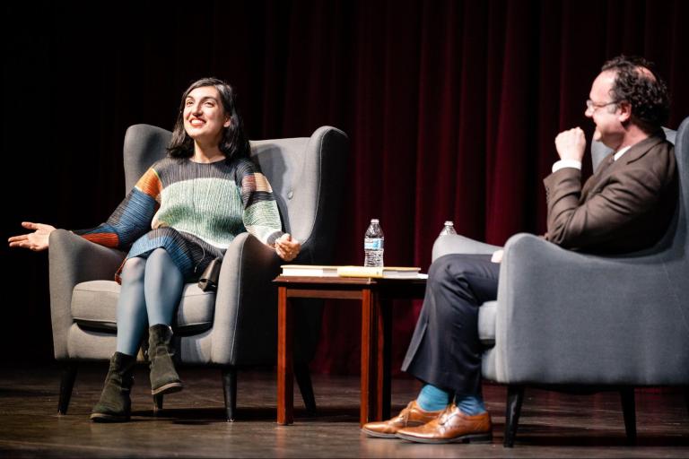 A woman having a conversation with a man in an auditorium.