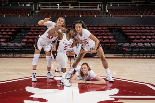 Three basketball players stand together with one player on the ground below them.