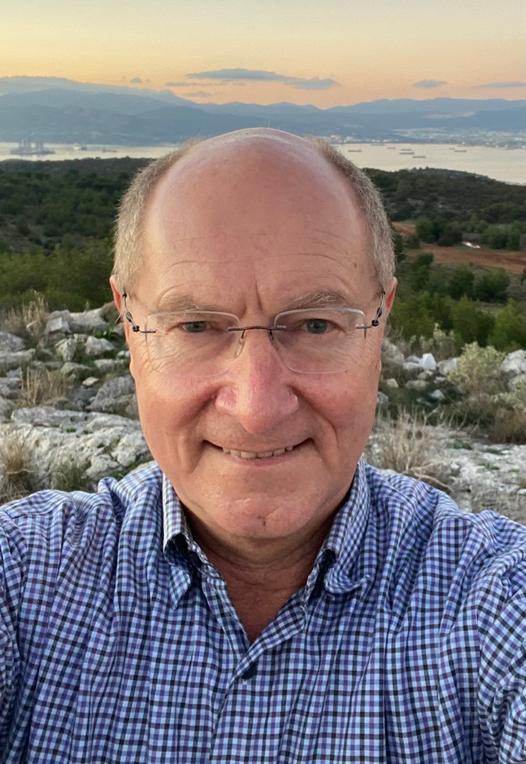 Picture of a man in a blue check shirt with a landscape background of grassy hills