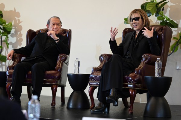 Yoshiki speaks to an audience with another panelist at the conference. Both are seated in armchairs, side by side.