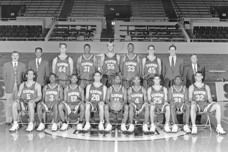 Men's basketball team stands in two rows, posing for their team photo.