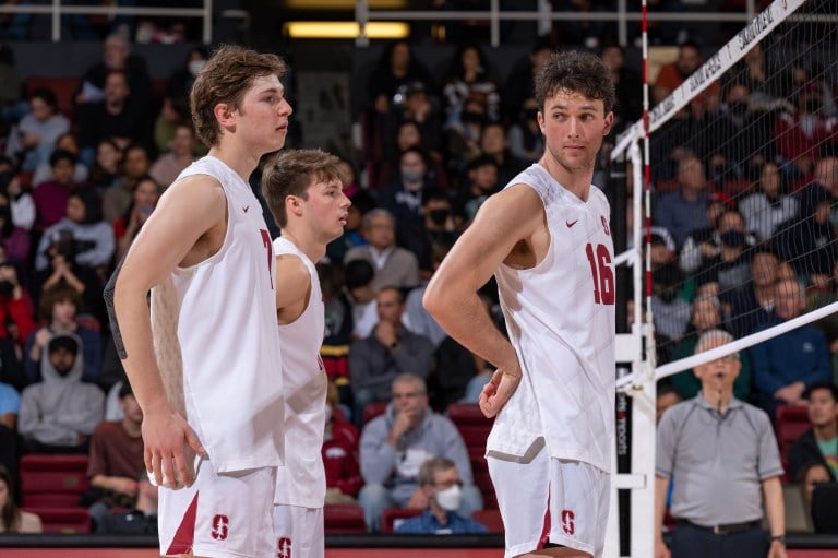 Three volleyball players stand at the net, waiting for the point to begin.