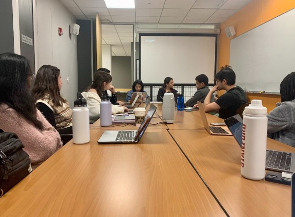 A group of Undergraduate senators sit around a table with their computers open on a black table.
