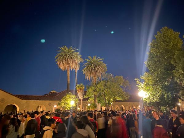 Main quad with students standing under lit up palm trees at night.