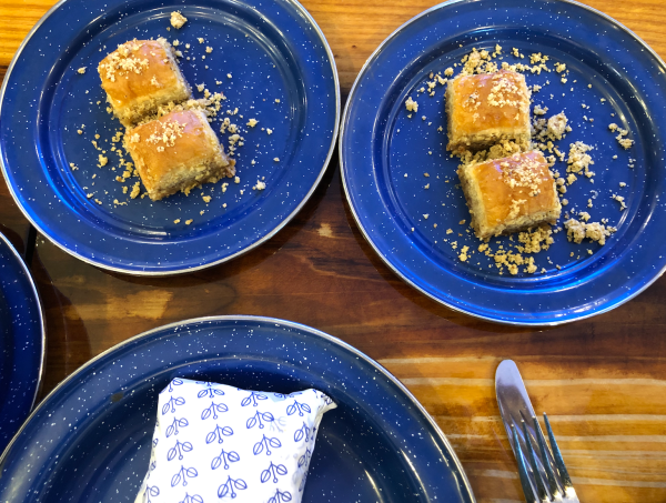 Two plates, each with two pieces of baklava sprinkled with pistachio crumbs, sit on speckled blue plates on a wooden table.