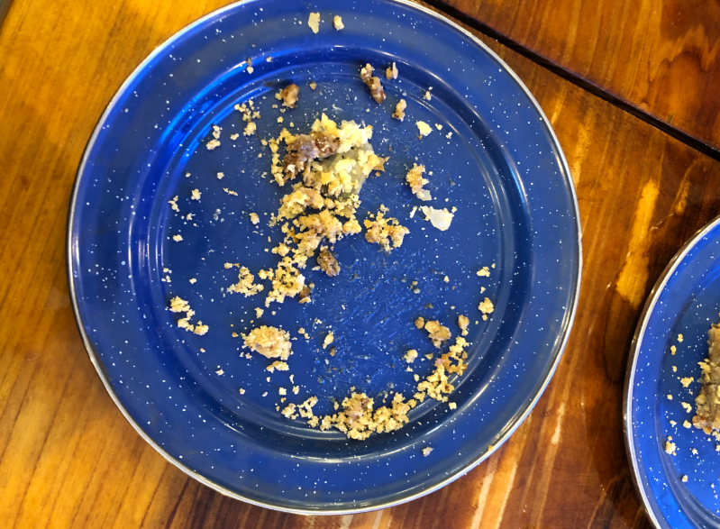 A speckled blue plate with baklava crumbs sits on a wooden table. 