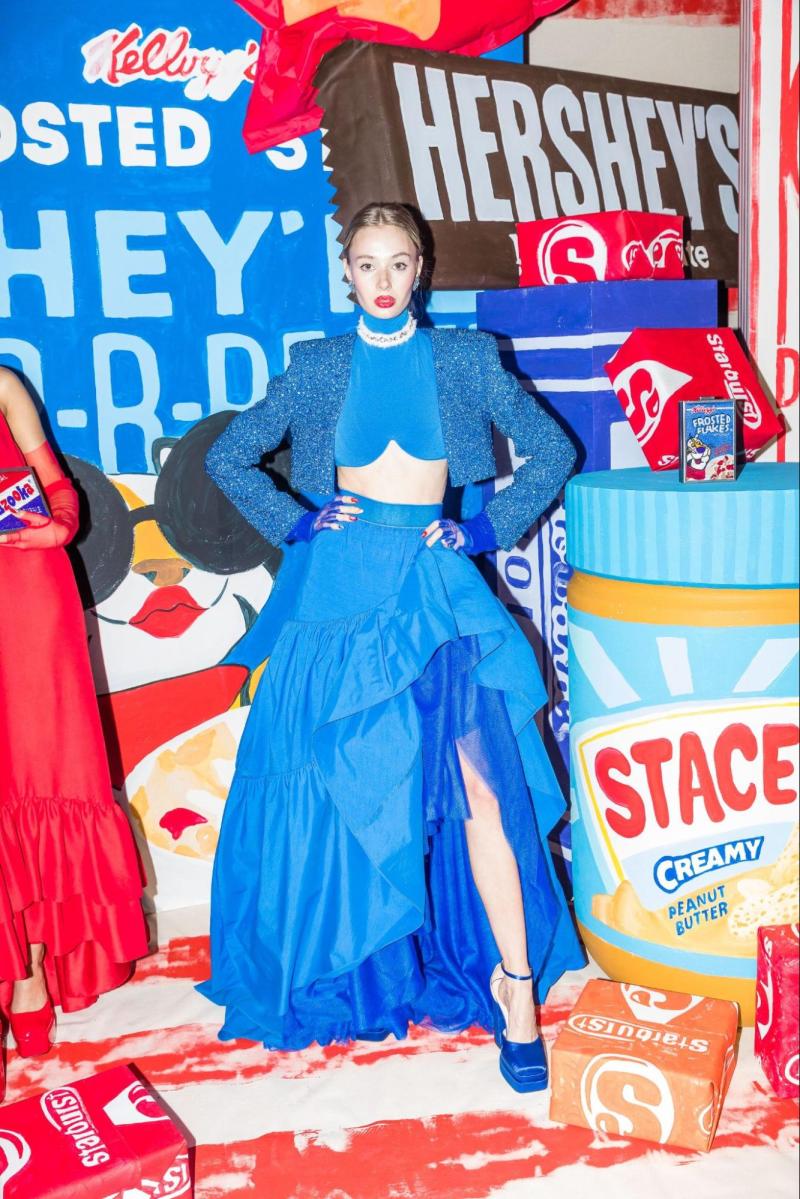 Model showcases a blue outfit in front of oversized starburst candies and a Jiffy peanut butter jar. 