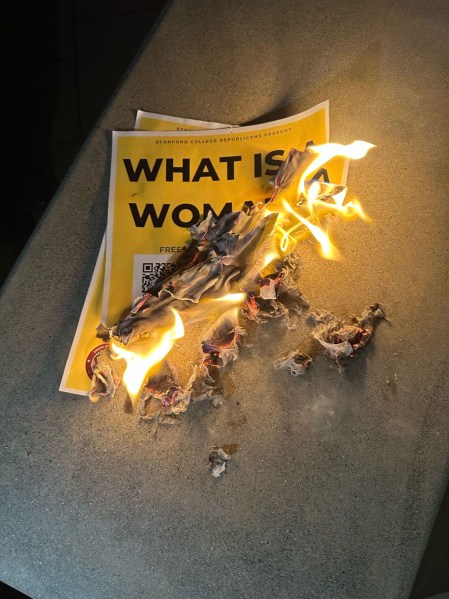 A flyer with the words "What is a Woman" is shown in flames and partly burned