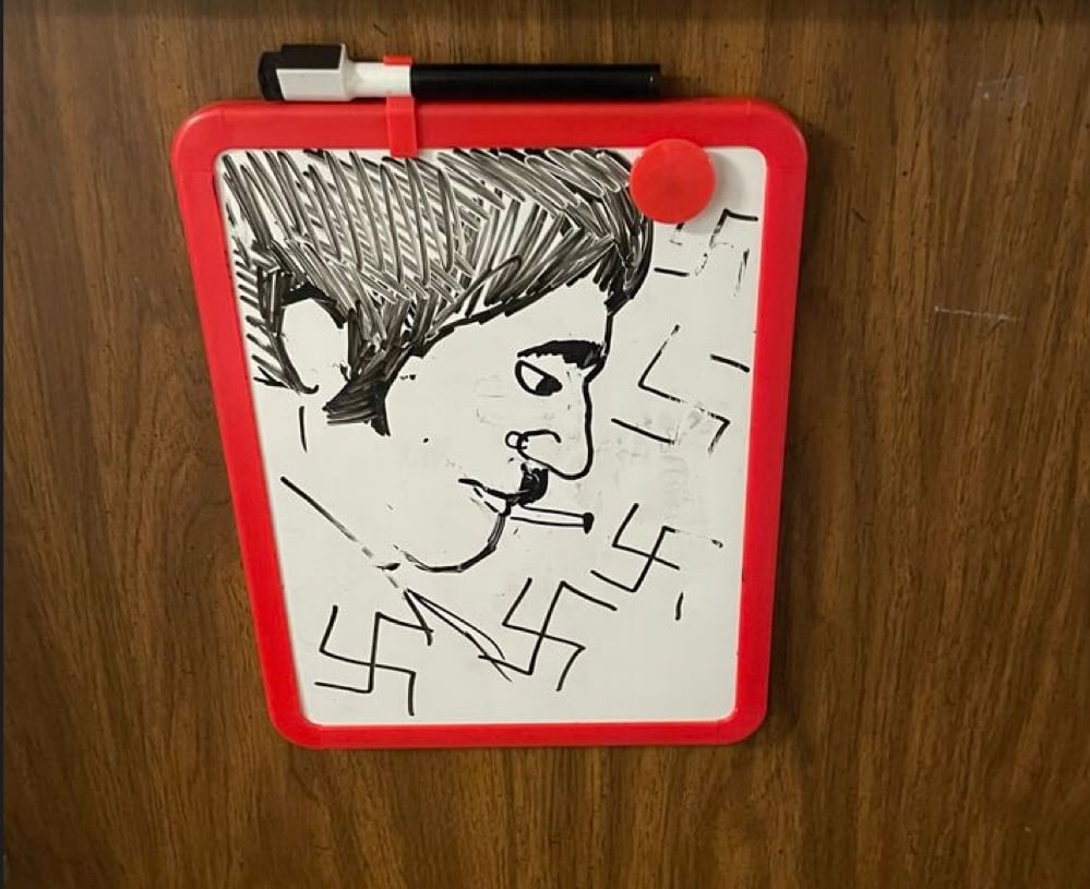 A drawing of a person resembling Hitler surrounded by swastikas on a whiteboard attached to a door