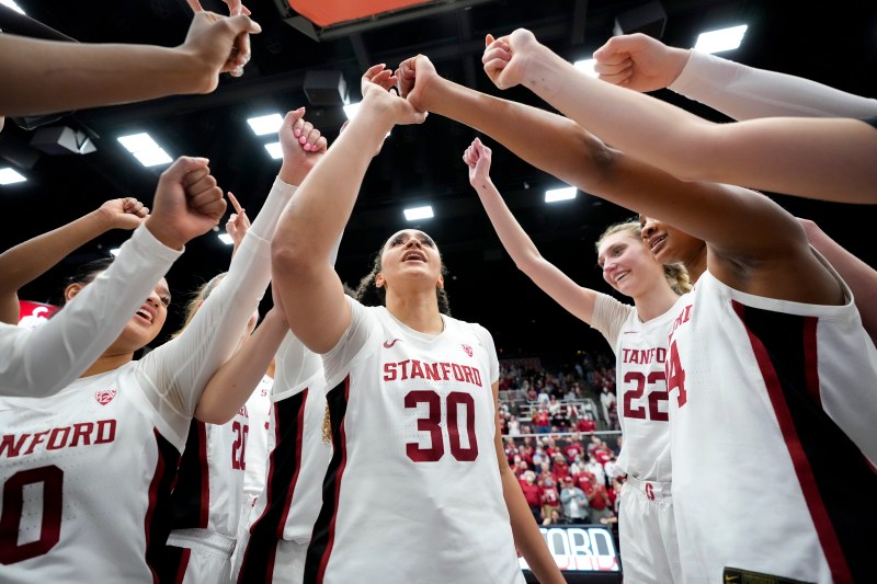 Women's basketball players raise their fists in the huddle.