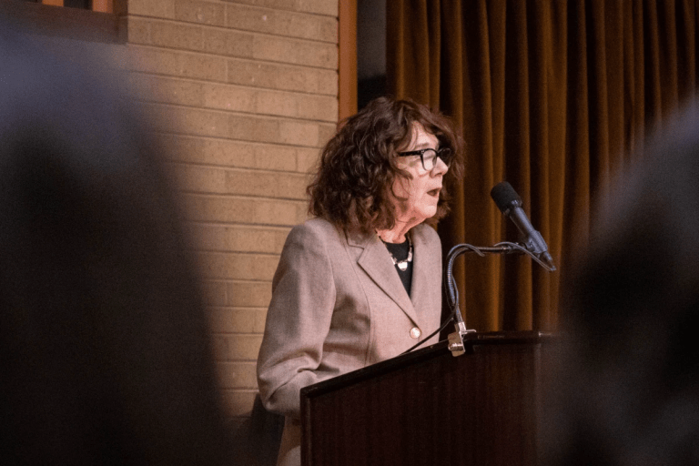 A closed-up shot of poet Mary Ruefle giving a reading against the background of dark curtains