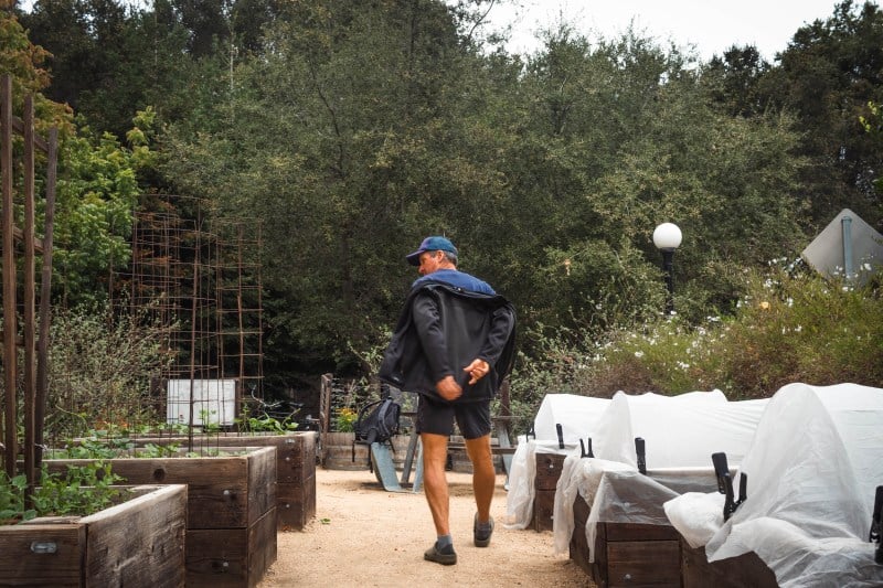 Conrad walks between rows of raised garden beds, some covered by plastic to protect the plants from the cold.