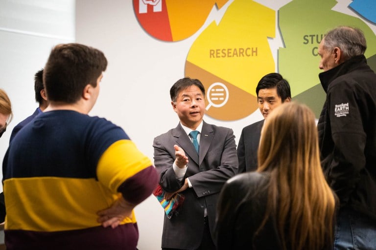 People stand in front of a man, listening to him talk.