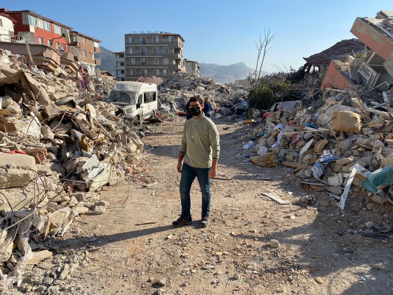 A man stands in the middle of a road with ruins on either side of him