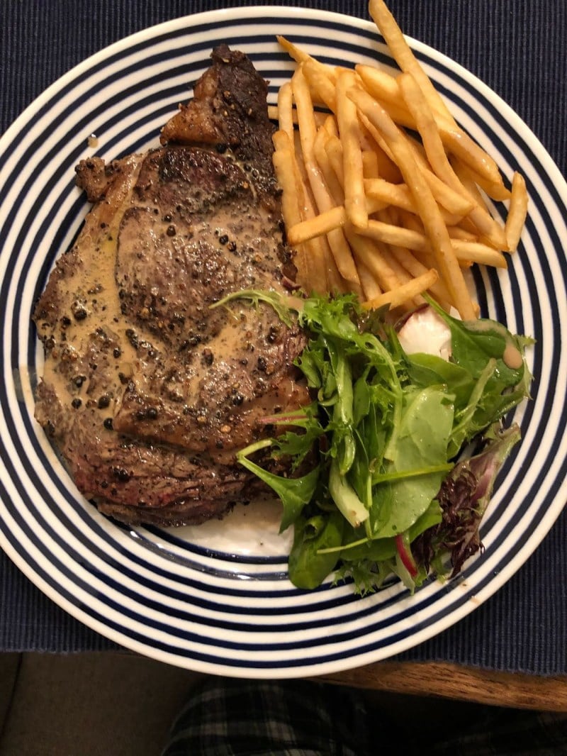 Steak Au Poivre, fries, and frisee salad sit on a plate.