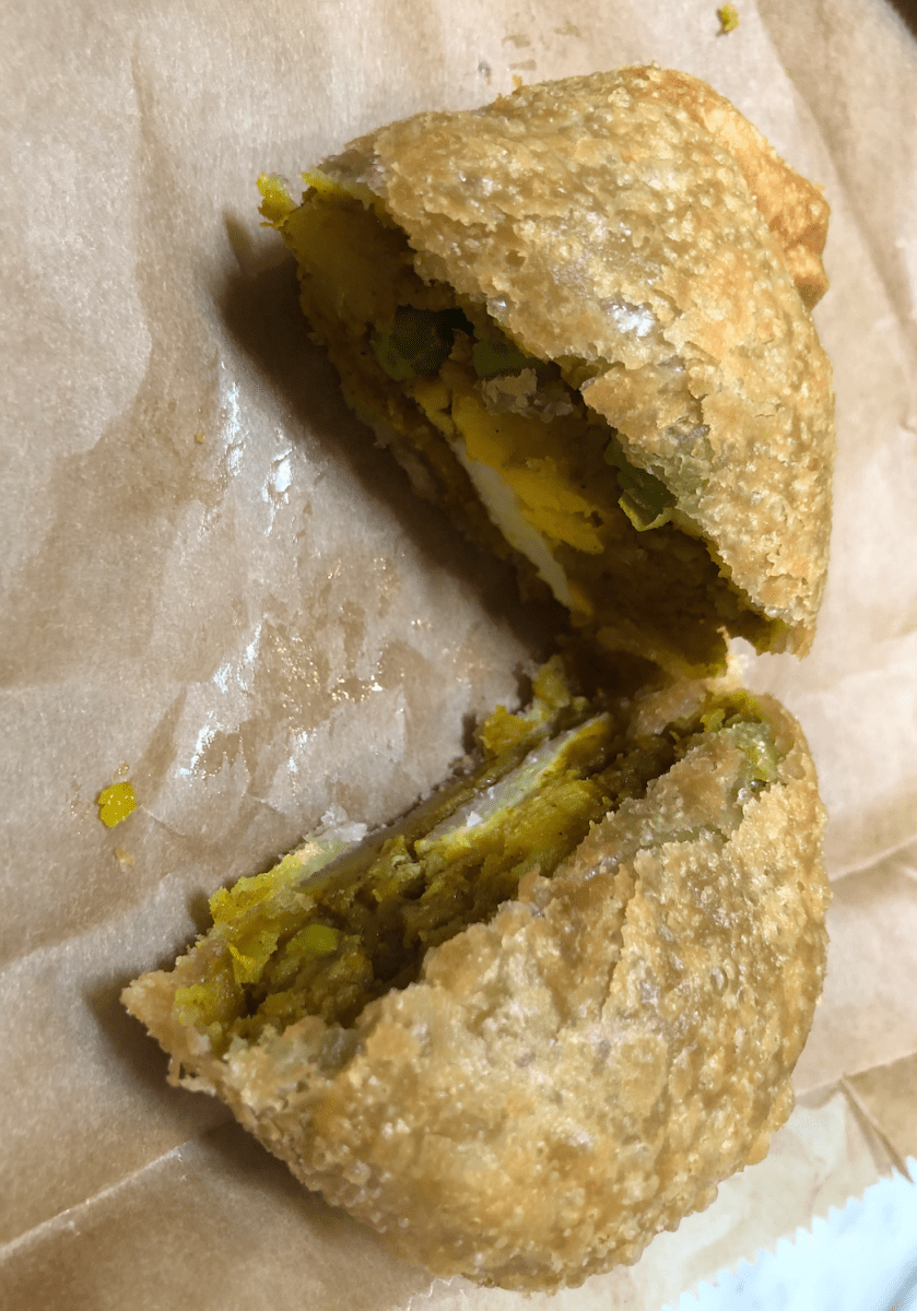 A potato curry puff cut in half shows off the soft green insides.