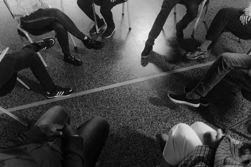 Black and white photo of people sitting in a circle, each with a foot in.