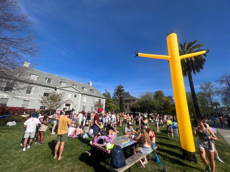 Students gathering on a lawn in front of a fraternity house.