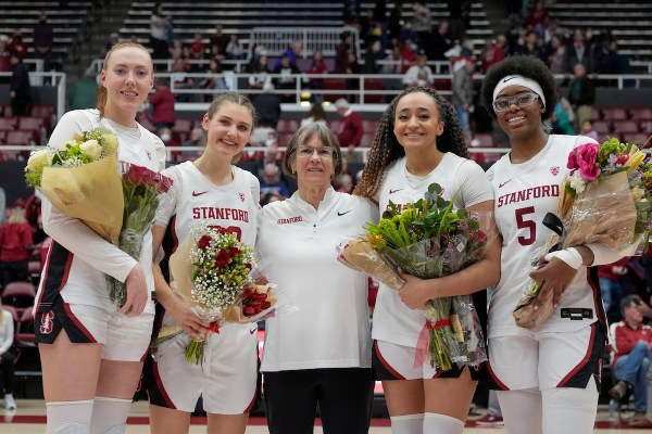 Four women basketball players stand with coach - two players on each side - with flowers in hand.