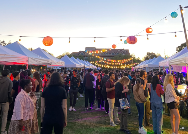 Lanterns are strung over booths of food and student artists as crowds of people mill around SunSet Fest.