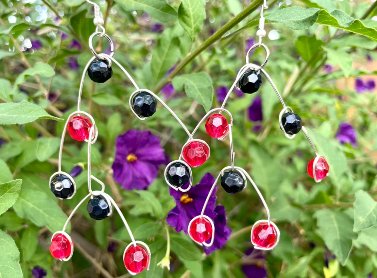 Earrings of red and black beads hang against a lush background. 