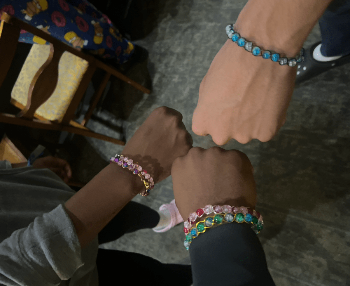 Three Ujama residents wearing beaded bracelets and holding their fists in a circle.