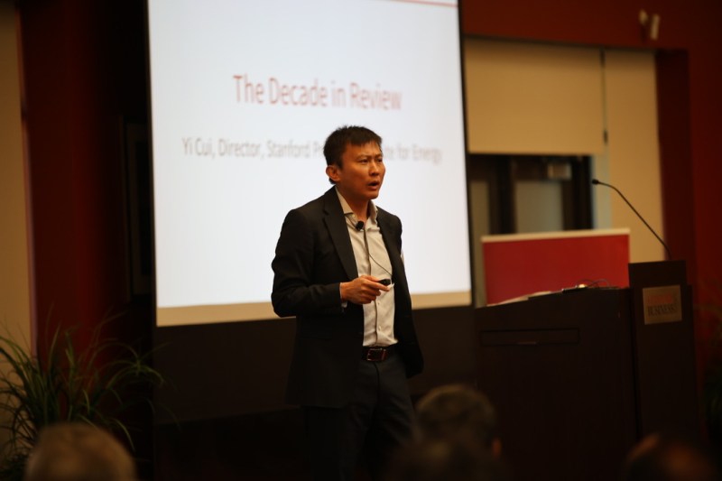 Yi Cui in front of a podium at an indoor event. An empty slide behind him reads "The Decade in Review"