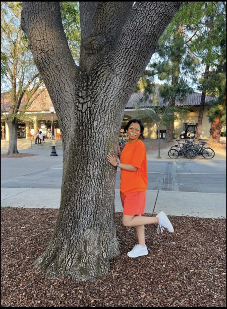 a person wearing a bright orange t-shirt and orange skin paint hugs a tree trunk