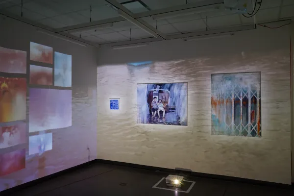 A wall of paintings with water projected in the background.