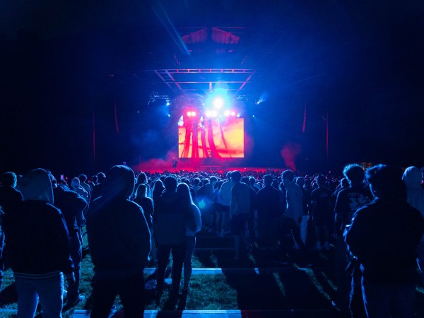 A crowd is shrouded in blue light and looking on at a red stage.