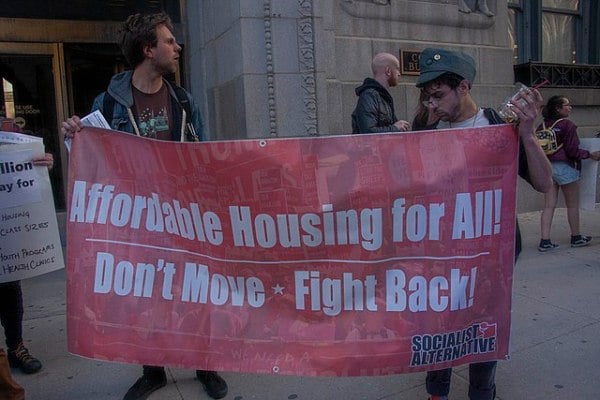 two men holding a sign that says, "Affordable Housing for All. Don't Move -- Fight Back"