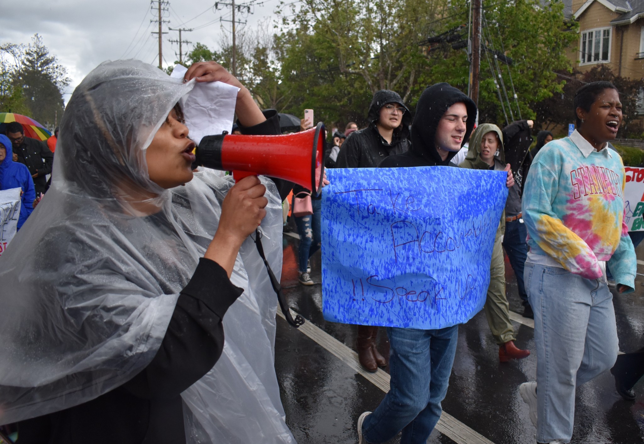Protestors march in the rain. One holds a sign; another holds a megaphone.