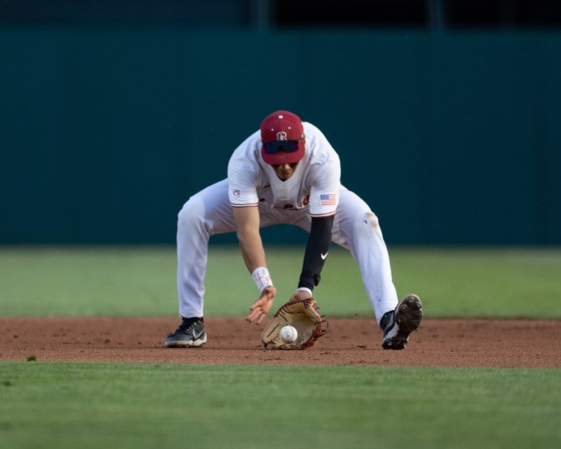 A baseball player crouches with his mitt towards the ground to field a ground ball during a baseball game.