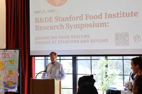 People look at a slide that reads "R&DE Stanford Food Institute Research Symposium: ADVANCING FOOD SYSTEMS CHANGE AT STANFORD AND BEYOND"