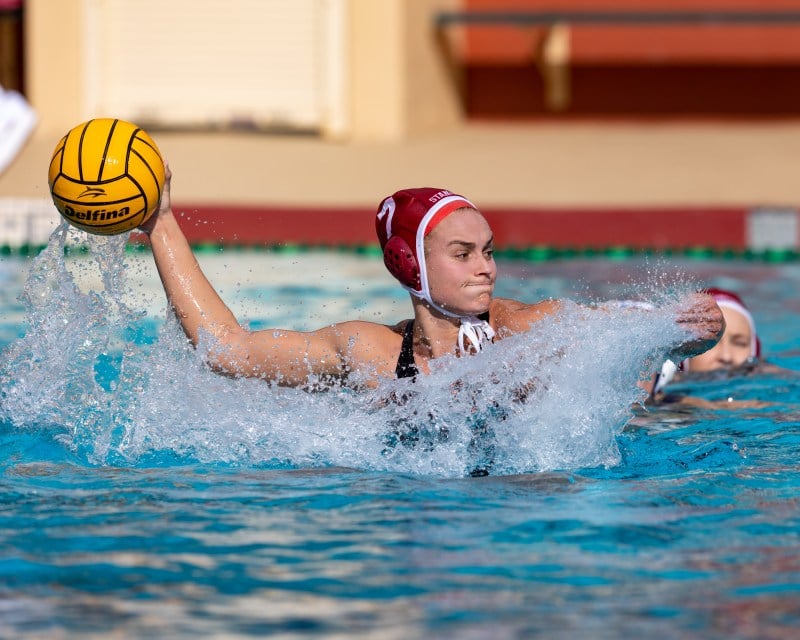 A water poloist winds up to pass during a game, with water splashing around her.