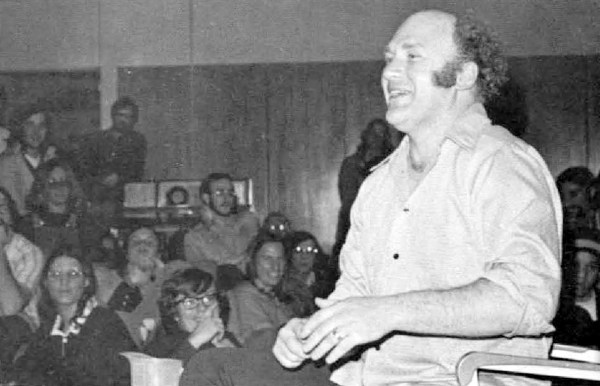 A black and white photo of Ken Kesey speaking to a group of students.